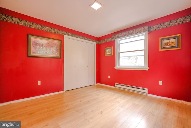 unfurnished bedroom featuring light wood-type flooring, baseboard heating, and a closet