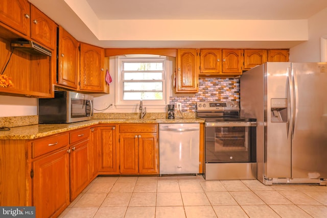 kitchen featuring light stone countertops, sink, stainless steel appliances, backsplash, and light tile patterned floors