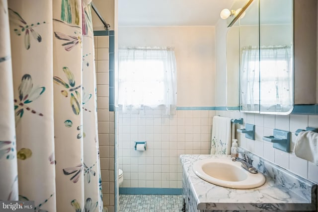 bathroom with a healthy amount of sunlight, toilet, sink, and tile walls