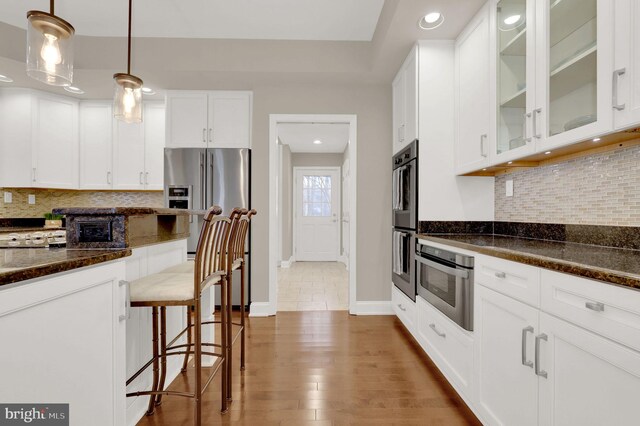 kitchen with dark hardwood / wood-style flooring, dark stone counters, white cabinetry, hanging light fixtures, and a breakfast bar area