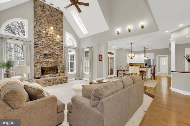 living room featuring decorative columns, ceiling fan with notable chandelier, light hardwood / wood-style flooring, high vaulted ceiling, and a stone fireplace