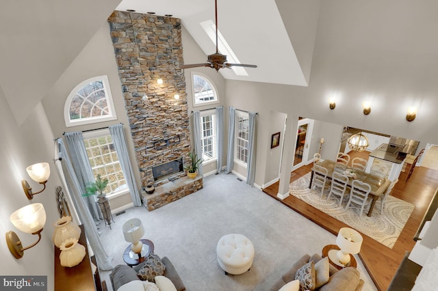 carpeted living room with ceiling fan with notable chandelier, a healthy amount of sunlight, a fireplace, and high vaulted ceiling