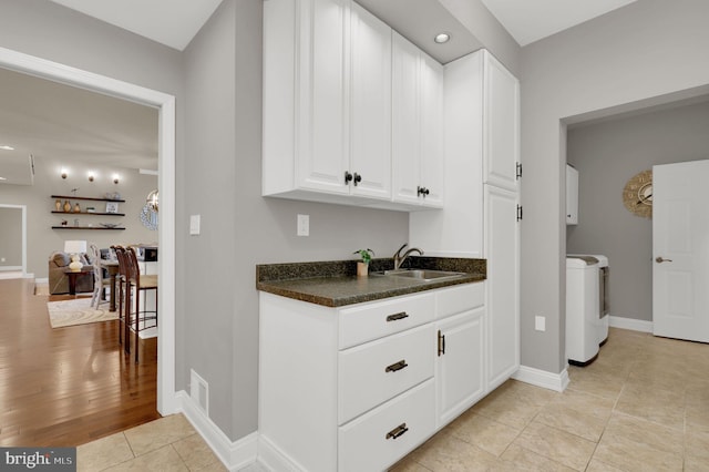 bar featuring white cabinets, independent washer and dryer, light wood-type flooring, and sink