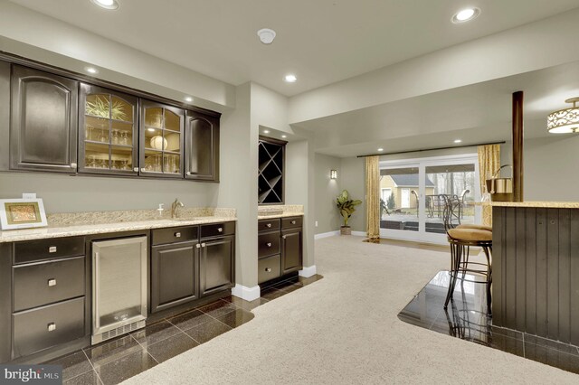 bar with dark carpet, sink, light stone countertops, dark brown cabinetry, and beverage cooler