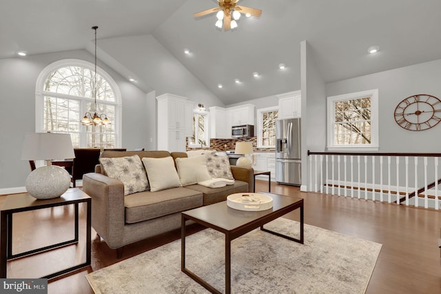 living room with ceiling fan with notable chandelier, high vaulted ceiling, and dark hardwood / wood-style floors