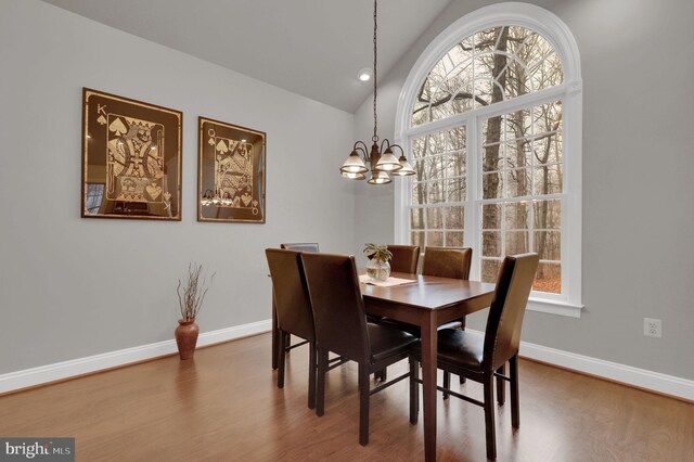 dining space with hardwood / wood-style flooring, an inviting chandelier, and vaulted ceiling