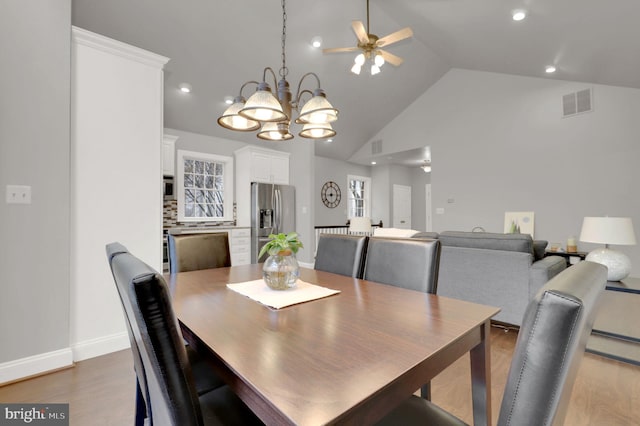 dining area with high vaulted ceiling, wood-type flooring, and ceiling fan with notable chandelier