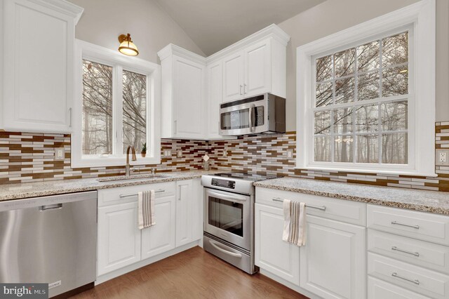 kitchen with appliances with stainless steel finishes, sink, hardwood / wood-style flooring, white cabinets, and lofted ceiling