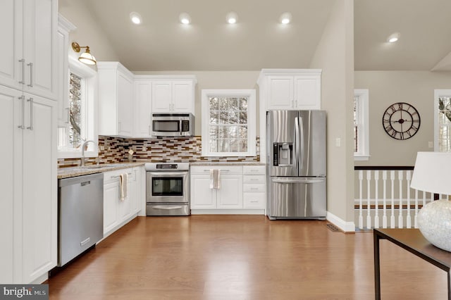 kitchen featuring appliances with stainless steel finishes, white cabinetry, vaulted ceiling, and hardwood / wood-style floors