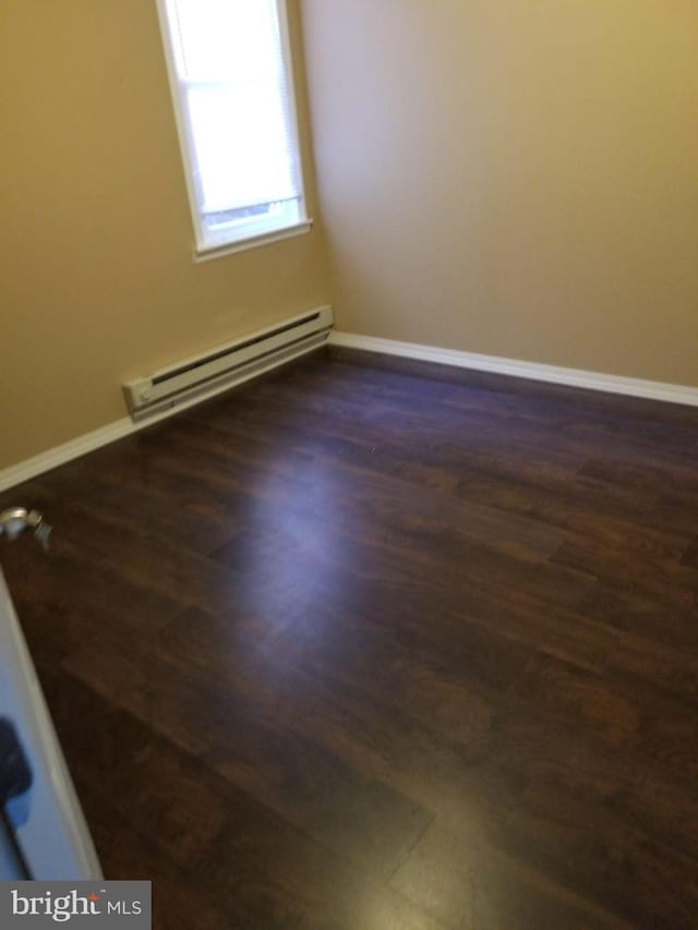 empty room featuring dark hardwood / wood-style flooring and a baseboard heating unit