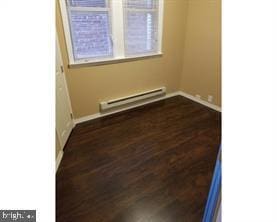 unfurnished room featuring dark hardwood / wood-style flooring and a baseboard heating unit