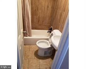 bathroom with tile patterned floors, toilet, shower / bath combo with shower curtain, and wooden walls