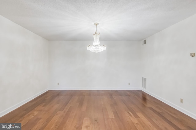 empty room featuring hardwood / wood-style floors, a textured ceiling, and an inviting chandelier