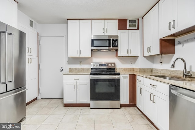 kitchen featuring light stone countertops, appliances with stainless steel finishes, a textured ceiling, sink, and white cabinetry