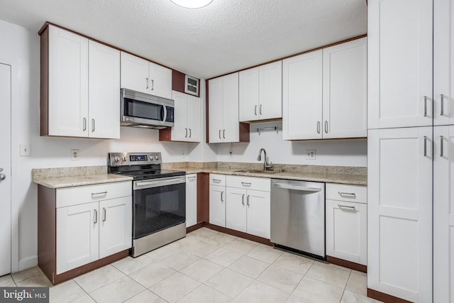 kitchen featuring white cabinets, sink, light tile patterned floors, a textured ceiling, and stainless steel appliances