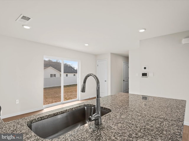 kitchen featuring wood-type flooring, dark stone counters, and sink