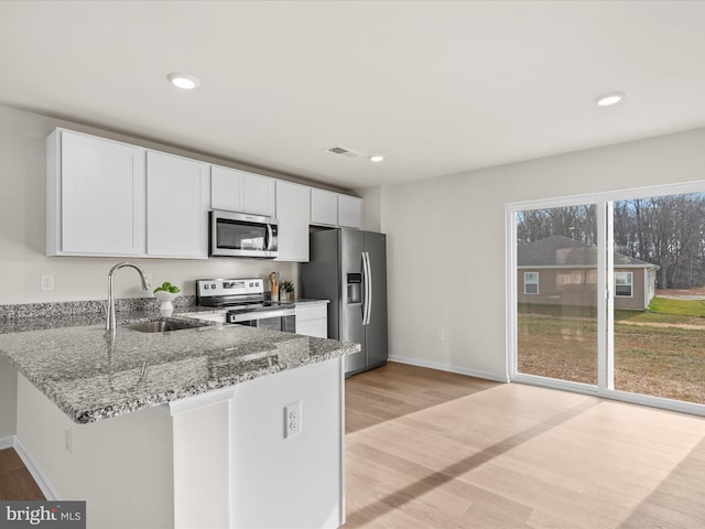 kitchen with white cabinets, sink, light stone countertops, light hardwood / wood-style floors, and stainless steel appliances