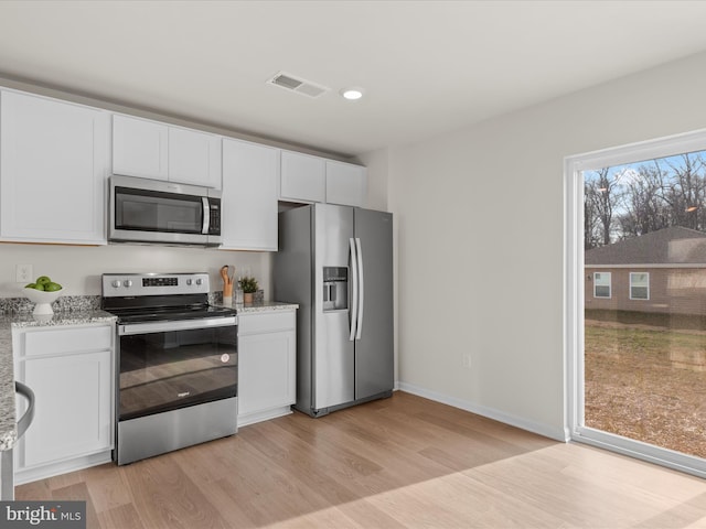 kitchen with white cabinets, light wood-type flooring, stainless steel appliances, and light stone counters