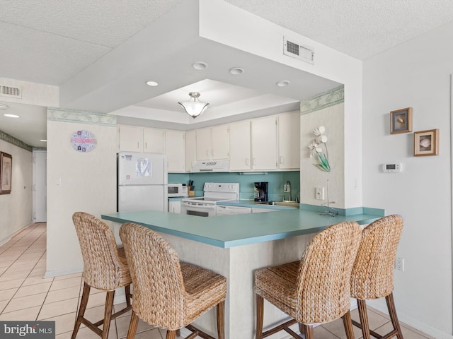 kitchen with kitchen peninsula, white appliances, sink, light tile patterned floors, and white cabinetry