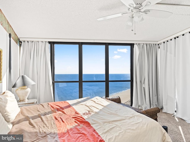 carpeted bedroom with ceiling fan, a water view, a textured ceiling, and a wall of windows