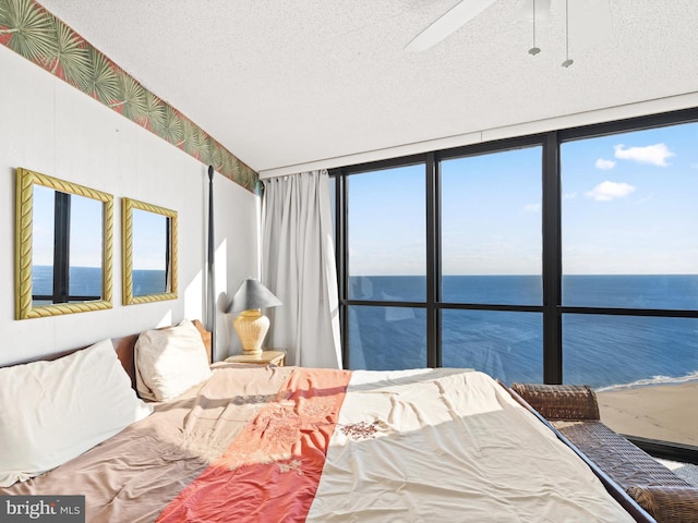 bedroom featuring multiple windows, ceiling fan, a water view, and a textured ceiling