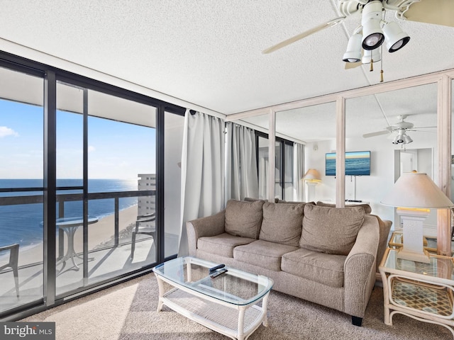 carpeted living room with floor to ceiling windows, a textured ceiling, ceiling fan, a view of the beach, and a water view