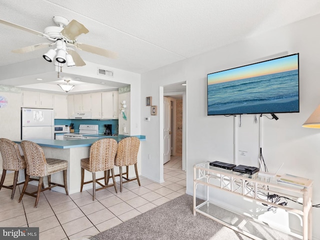 kitchen with white appliances, white cabinets, ceiling fan, light tile patterned floors, and a breakfast bar area