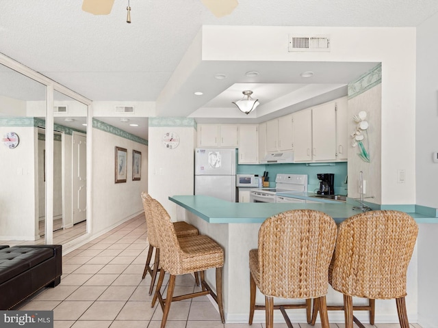 kitchen featuring white appliances, a kitchen breakfast bar, kitchen peninsula, white cabinetry, and extractor fan