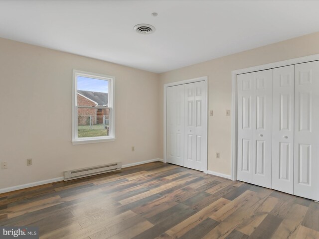 unfurnished bedroom with dark hardwood / wood-style flooring, multiple closets, and a baseboard heating unit