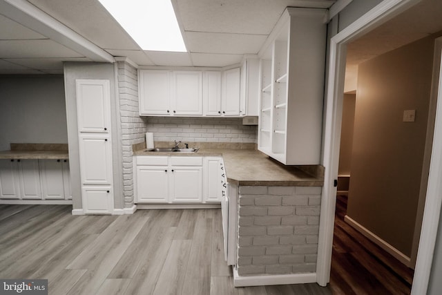 kitchen with white cabinetry, a drop ceiling, sink, light hardwood / wood-style flooring, and backsplash