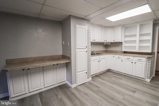 kitchen featuring a drop ceiling, tasteful backsplash, white cabinetry, and light hardwood / wood-style flooring