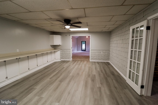 empty room with ceiling fan, light hardwood / wood-style flooring, a drop ceiling, and brick wall