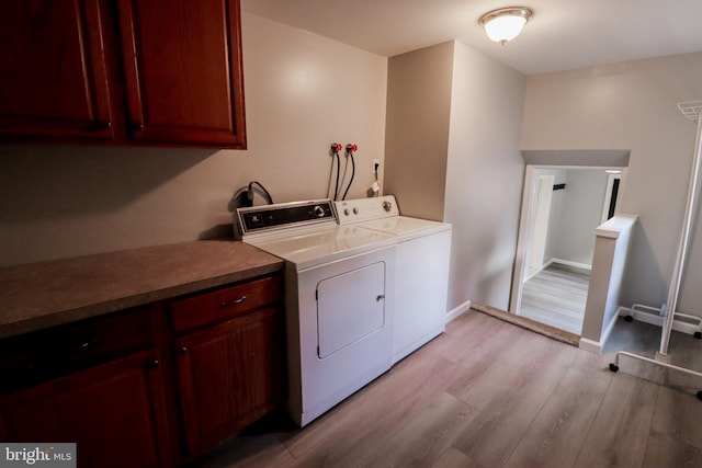 laundry room with cabinets, light wood-type flooring, and washer and clothes dryer