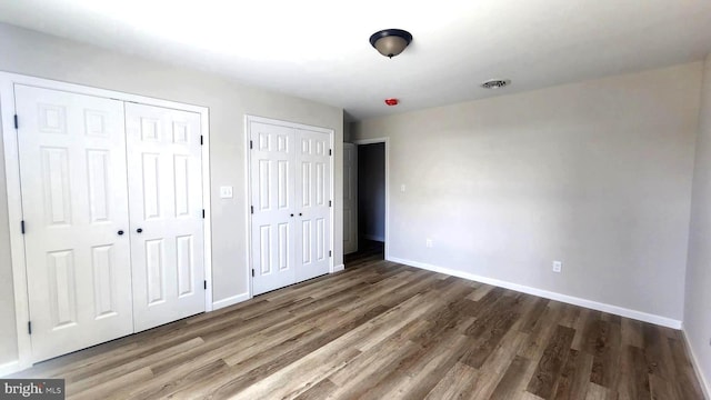 unfurnished bedroom with dark wood-type flooring and two closets