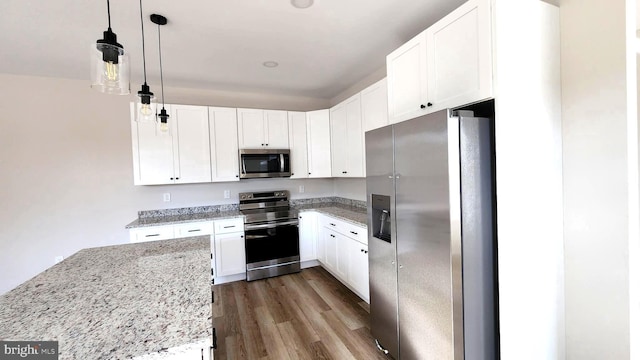 kitchen with hanging light fixtures, dark wood-type flooring, stainless steel appliances, light stone counters, and white cabinets