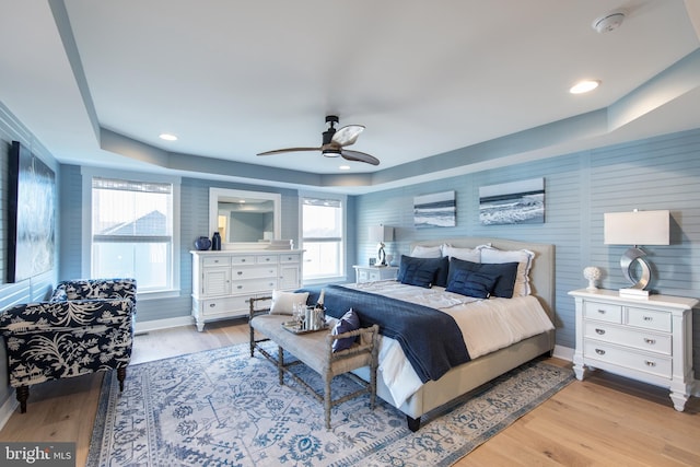 bedroom featuring a raised ceiling, ceiling fan, and light wood-type flooring