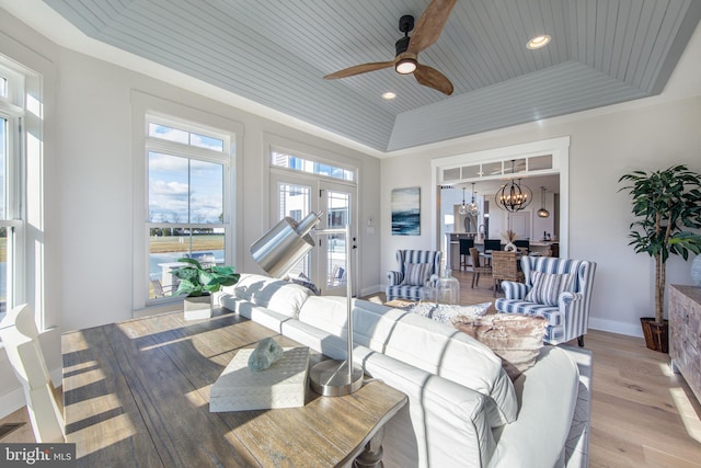 living room featuring ceiling fan with notable chandelier, light hardwood / wood-style flooring, a raised ceiling, and wooden ceiling