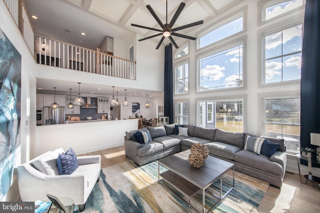 living room with coffered ceiling, ceiling fan, beam ceiling, a high ceiling, and light hardwood / wood-style floors