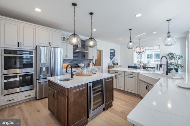 kitchen featuring a kitchen island with sink, white cabinets, hanging light fixtures, wine cooler, and stainless steel appliances