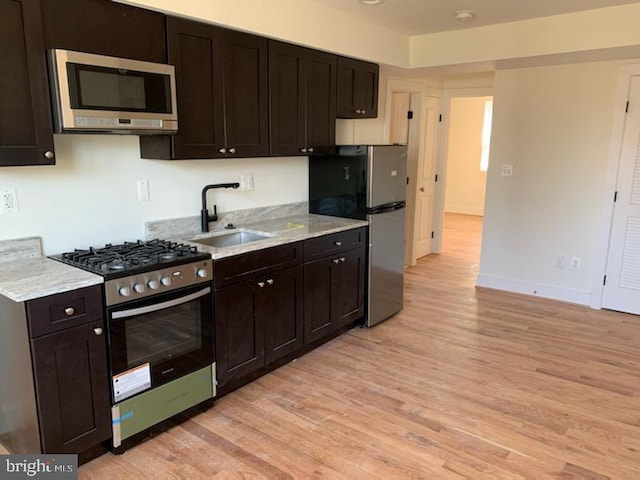 kitchen featuring sink, dark brown cabinetry, stainless steel appliances, and light hardwood / wood-style flooring