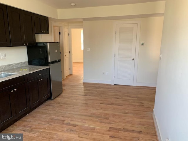 kitchen with dark brown cabinets, light hardwood / wood-style floors, and stainless steel refrigerator