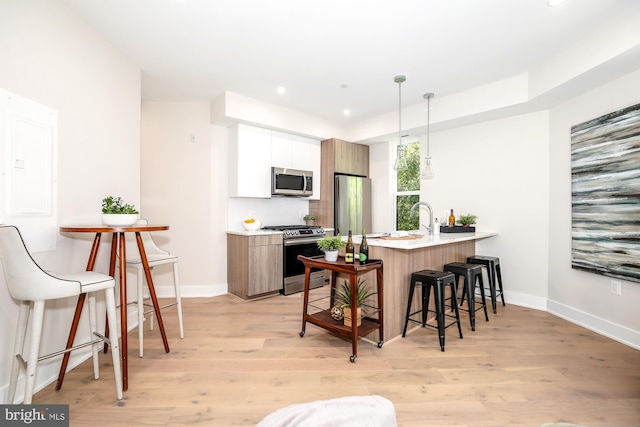 kitchen with kitchen peninsula, stainless steel appliances, white cabinetry, and light hardwood / wood-style flooring