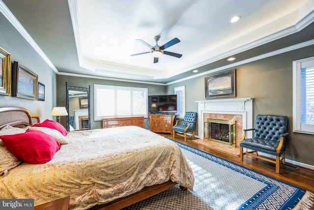 bedroom with wood-type flooring, ceiling fan, crown molding, and a premium fireplace