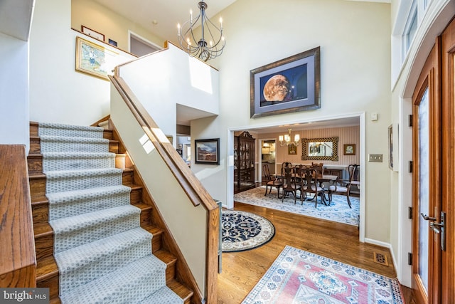 staircase with hardwood / wood-style flooring, a high ceiling, and an inviting chandelier