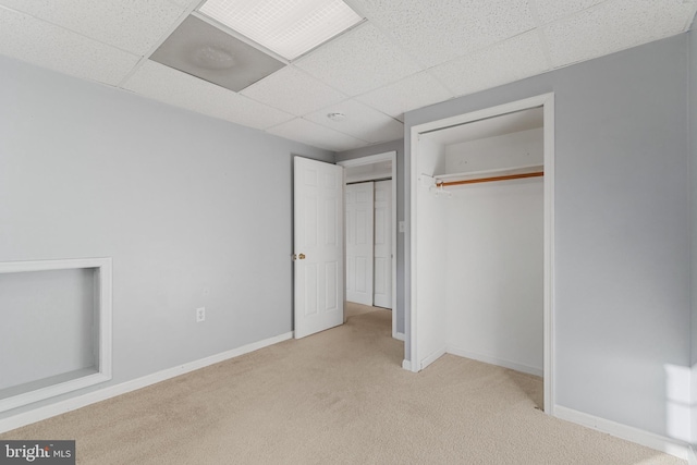 unfurnished bedroom featuring light carpet, a paneled ceiling, and a closet