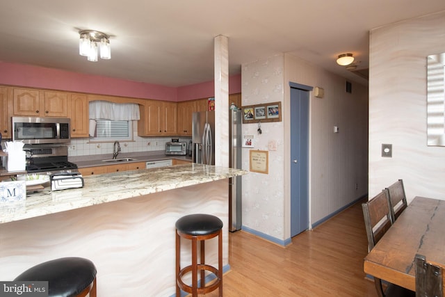 kitchen with light stone countertops, appliances with stainless steel finishes, light wood-type flooring, tasteful backsplash, and sink