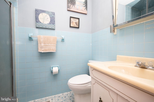 bathroom with tile patterned floors, vanity, a shower with door, tile walls, and toilet