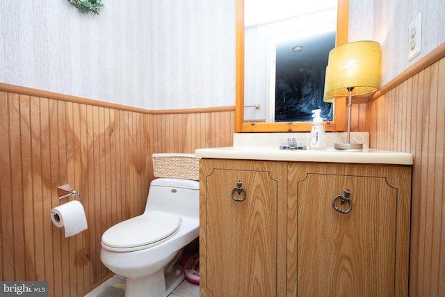 bathroom with wooden walls, tile patterned flooring, vanity, and toilet