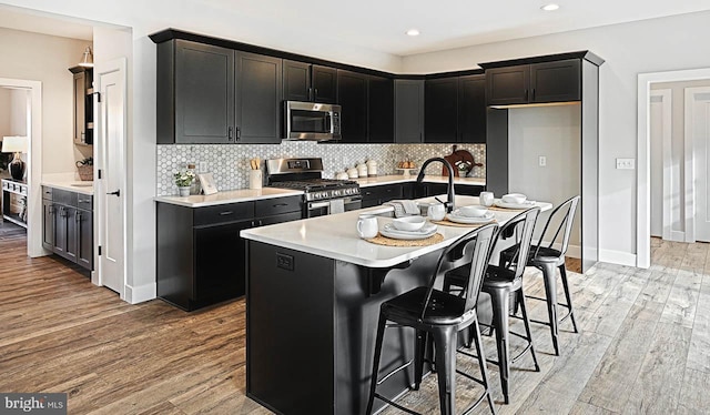 kitchen featuring stainless steel appliances, a kitchen breakfast bar, backsplash, light hardwood / wood-style floors, and a center island with sink