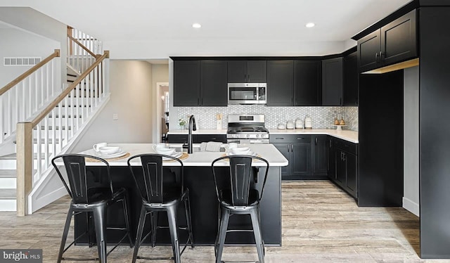 kitchen with a kitchen breakfast bar, a kitchen island with sink, light hardwood / wood-style floors, and appliances with stainless steel finishes